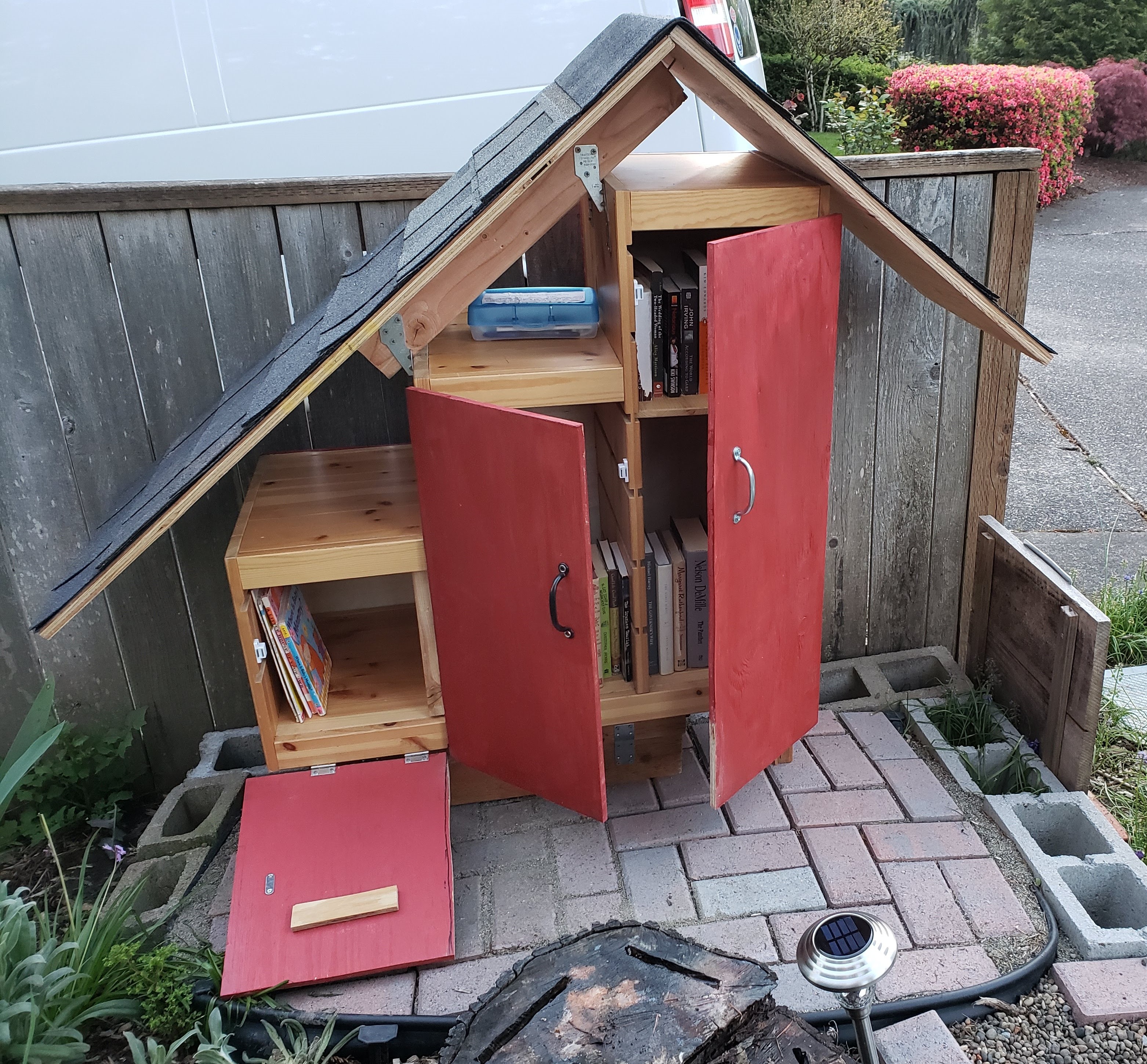 Front view of the Little Free Library, with the doors open - showing that they each open in a different direction, and giving a peek at the books inside.